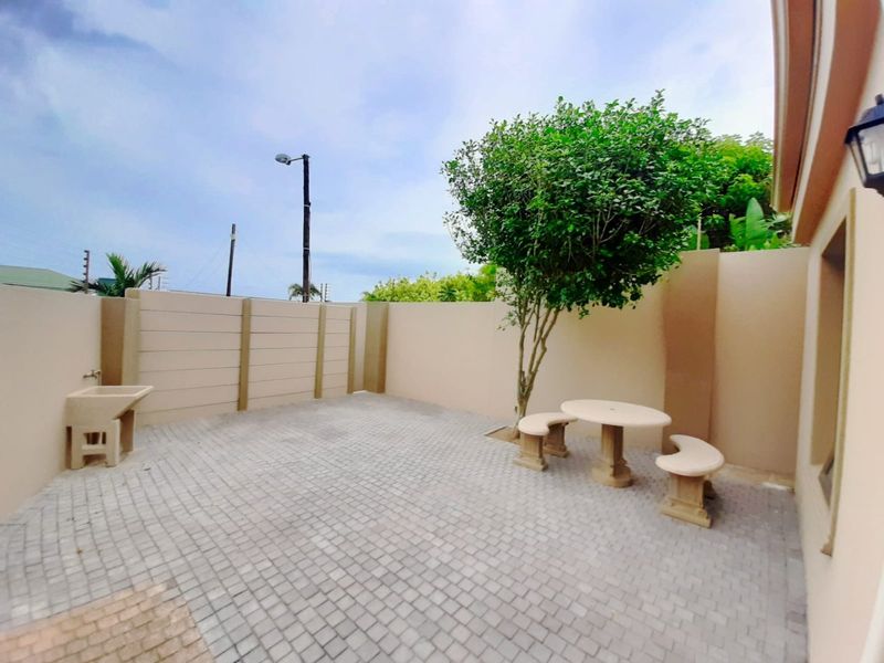 A private paved patio area featuring a boundary wall, utility sink, and established tree, providing a functional outdoor space.