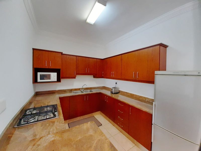 A functional kitchen featuring warm-toned wooden cabinetry, stone countertops, a gas hob, and a double sink, offering a practical layout for daily cooking.