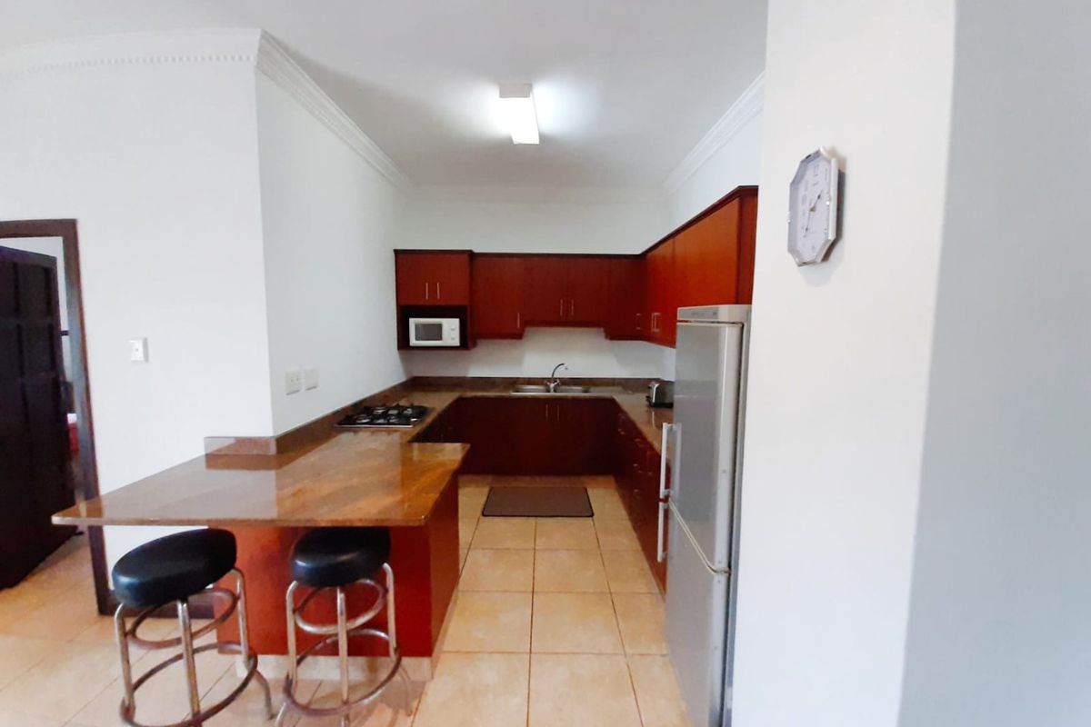 A functional kitchen featuring dark wood cabinetry, stone countertops, a breakfast bar, and a gas hob, with tiled flooring throughout.