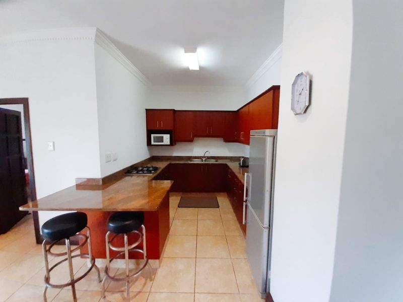 A functional kitchen featuring dark wood cabinetry, stone countertops, a breakfast bar, and a gas hob, with tiled flooring throughout.