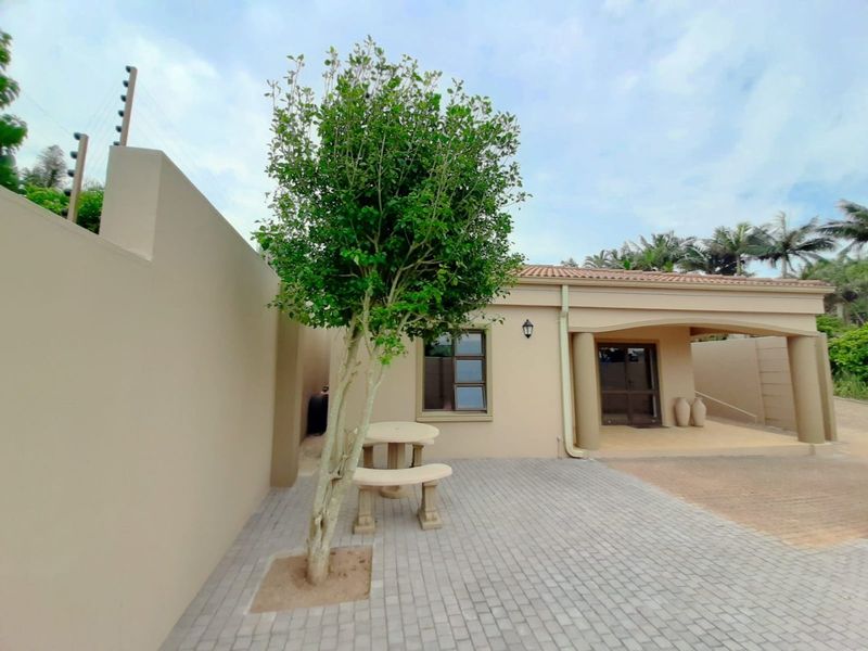 Front exterior view of the apartment featuring a paved driveway, covered entrance, and secure boundary wall with electric fencing.