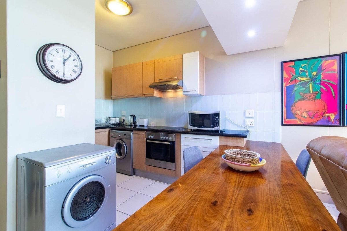 Open-plan kitchen area featuring built-in cabinetry, integrated oven and hob, tiled backsplash, and tiled flooring, seamlessly connected to the living space.