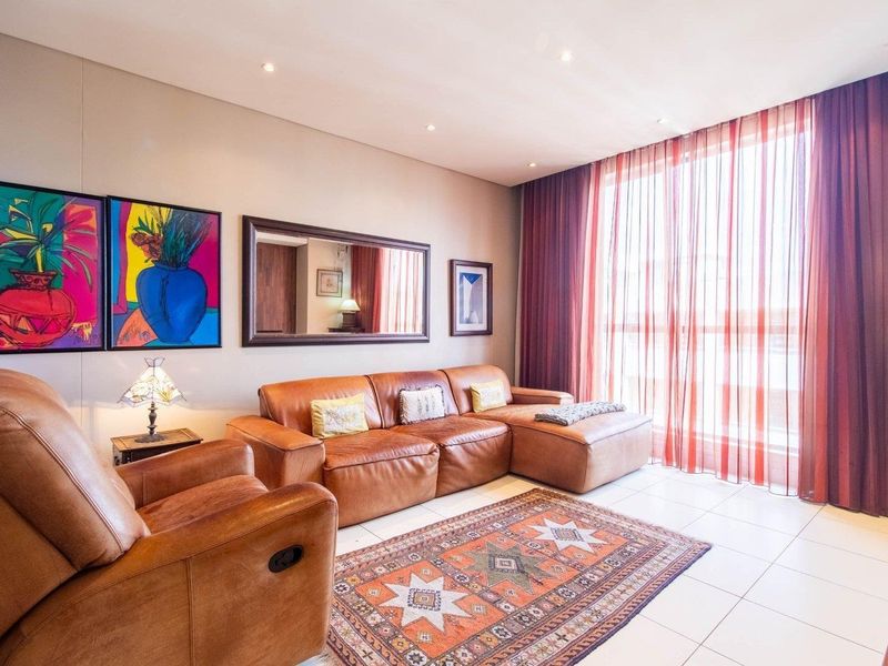 A well-lit living room featuring tiled flooring, recessed downlighting, and floor-to-ceiling curtains providing natural light.