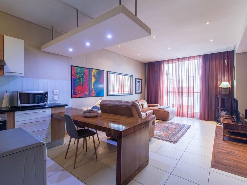 An open-plan living and kitchen area featuring tiled floors, modern cabinetry, integrated appliances, and large sliding doors leading to a balcony.