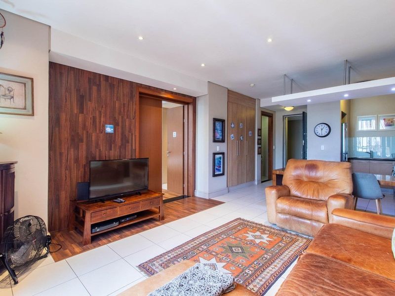 An open-plan living area featuring tiled floors, wood-paneled feature wall, and integrated kitchen cabinetry with recessed lighting throughout.