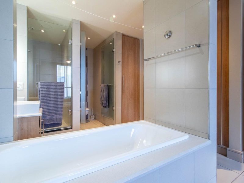 Modern bathroom featuring a built-in bathtub, separate glass-enclosed shower, and contemporary vanity cabinetry with neutral wall and floor tiling.