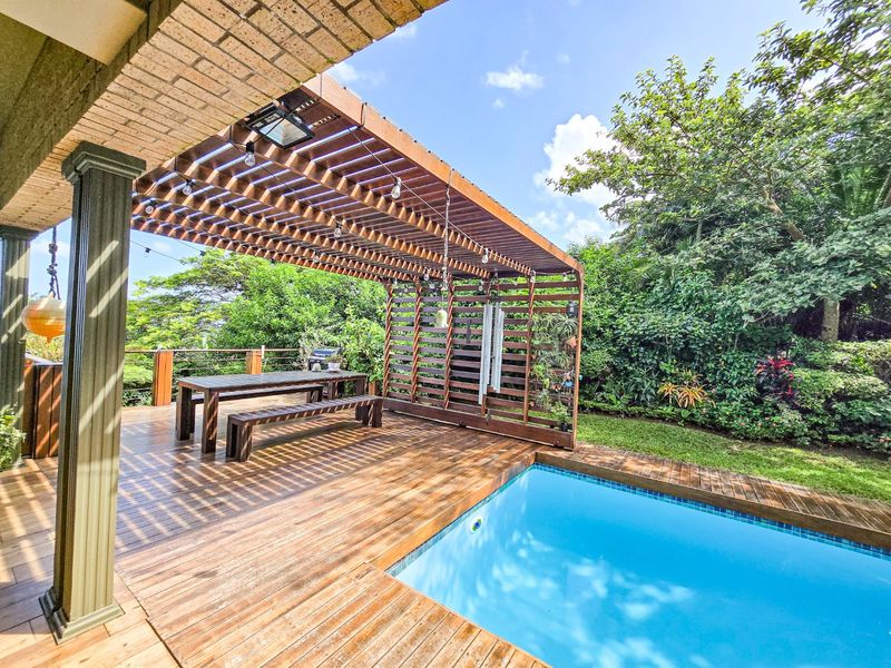 Outdoor entertainment area featuring a timber deck, swimming pool, and a large timber pergola, set within a lush garden environment.