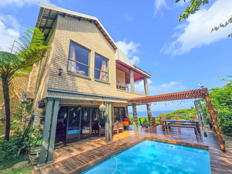 A beautiful outdoor entertainment area featuring a swimming pool, timber decking, and a pergola, set against a scenic coastal backdrop.