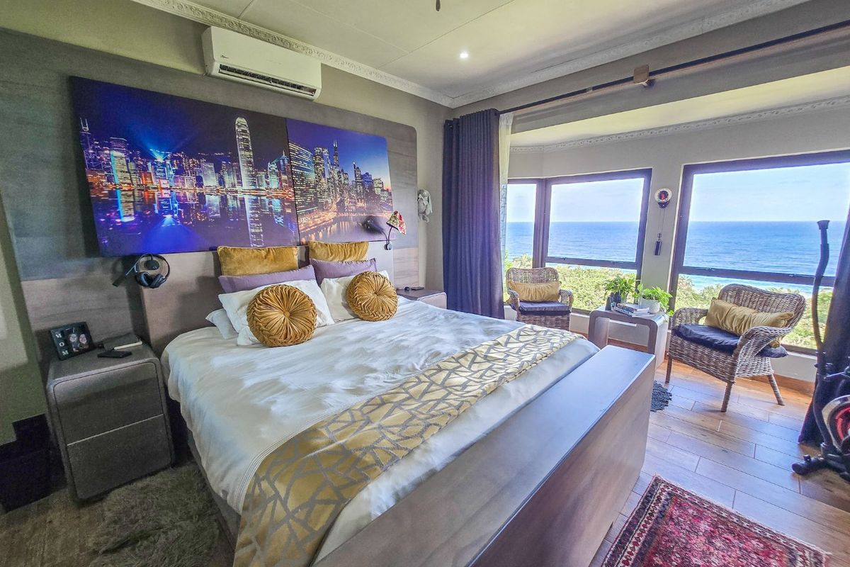 Spacious bedroom featuring wood-look tile flooring, decorative ceiling cornices, and large bay windows offering expansive ocean views.