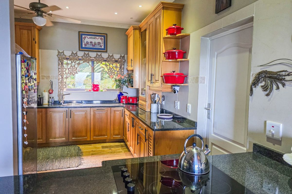 A functional kitchen featuring warm wooden cabinetry, dark granite countertops, an integrated electric hob, and recessed ceiling lighting.