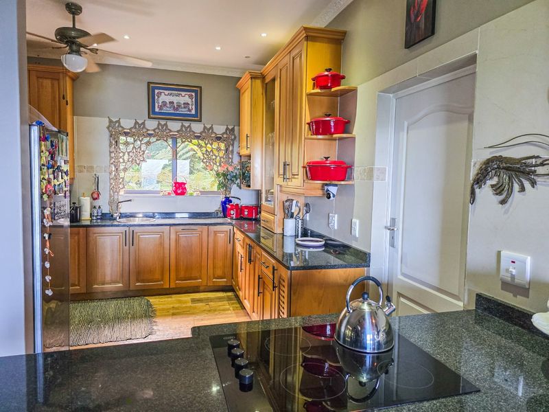 A functional kitchen featuring warm wooden cabinetry, dark granite countertops, an integrated electric hob, and recessed ceiling lighting.