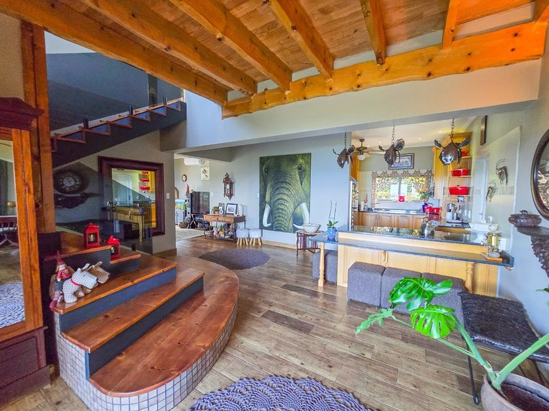 Spacious open-plan living area featuring exposed timber ceiling beams, a central timber staircase, and a well-appointed kitchen with granite countertops and timber cabinetry.
