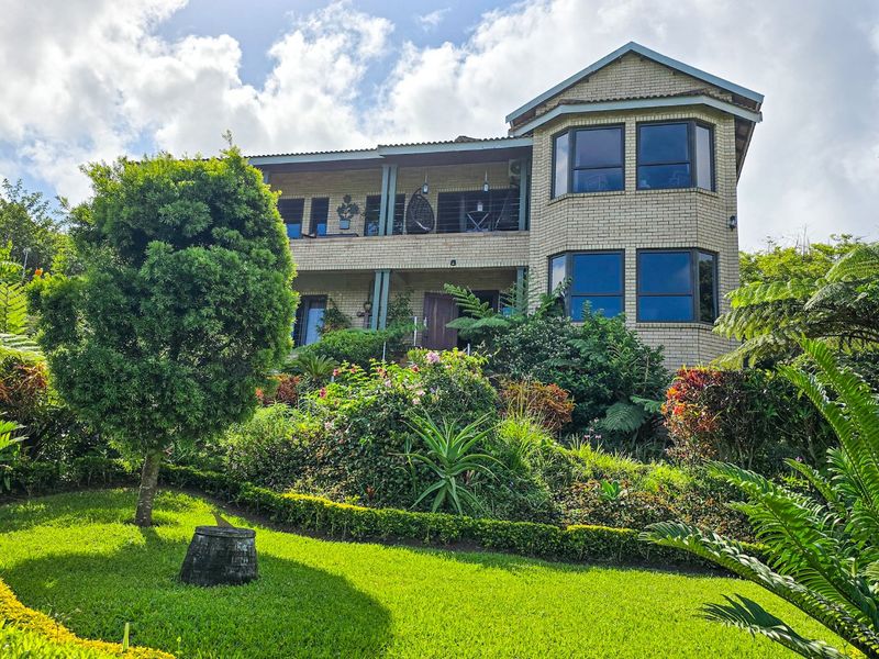 A two-story brick house featuring bay windows, a covered balcony, and a well-maintained landscaped garden in the foreground.