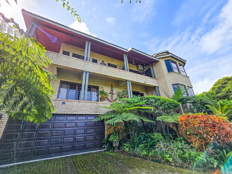 A multi-level brick residence featuring a spacious garage, tiered balconies, and established garden landscaping, presenting a classic architectural style.