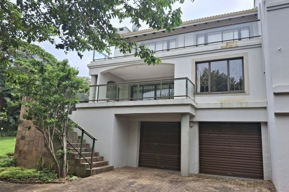 Rear view of a multi-level townhouse featuring a double garage, paved driveway, and upper-level balconies with glass balustrades.