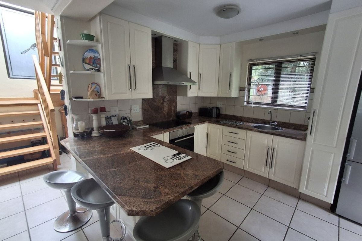 A functional kitchen featuring granite countertops, built-in appliances, tiled flooring, and an adjacent wooden staircase leading to the upper level.