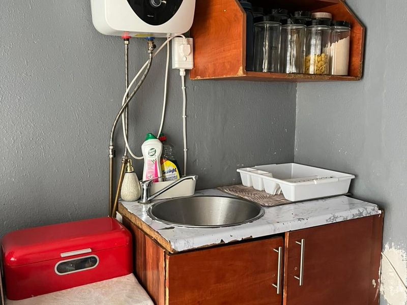 A compact scullery area featuring a stainless steel sink, built-in wooden cabinetry, and an electric water heater mounted on the wall.