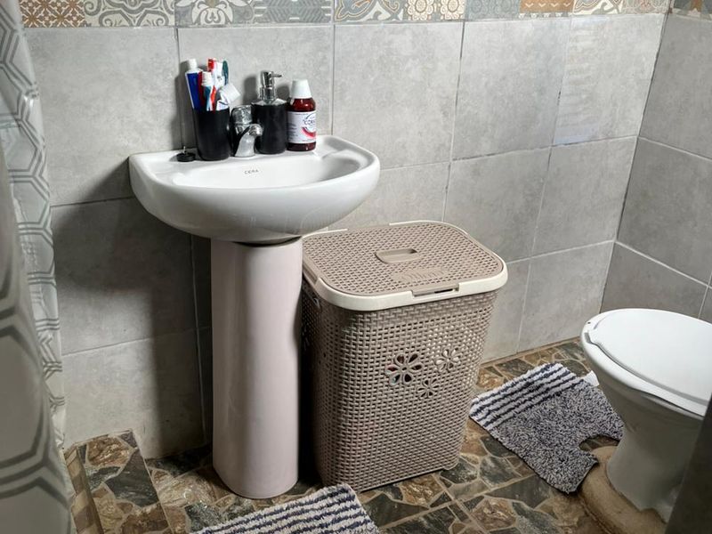 A compact bathroom featuring a pedestal basin, toilet, and decorative wall tiling with a patterned accent border.