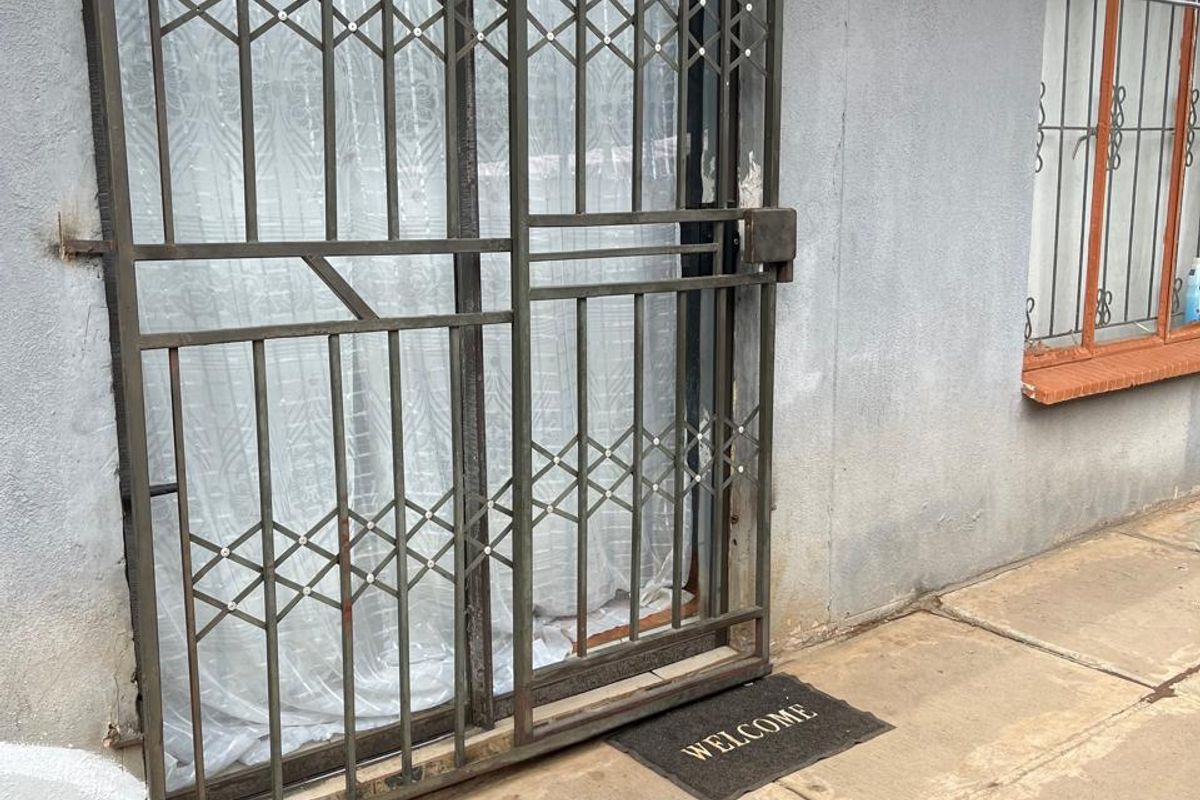 Rear exterior view of an apartment featuring a paved patio area, sliding glass door, and metal security gate with protective window bars.