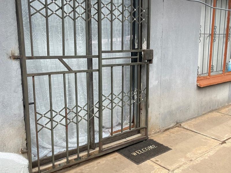 Rear exterior view of an apartment featuring a paved patio area, sliding glass door, and metal security gate with protective window bars.