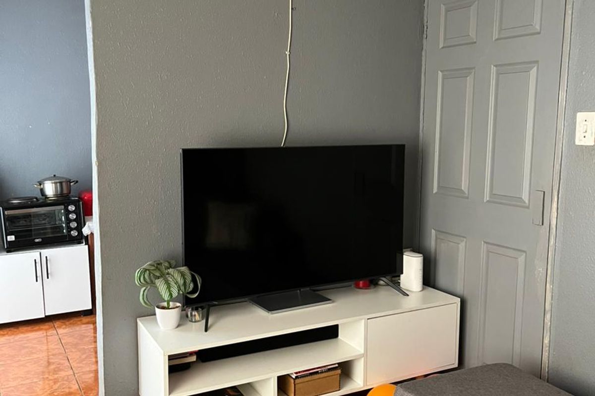 A living room area featuring tiled flooring and a panel door, with visible ceiling trim and electrical wiring requiring maintenance.