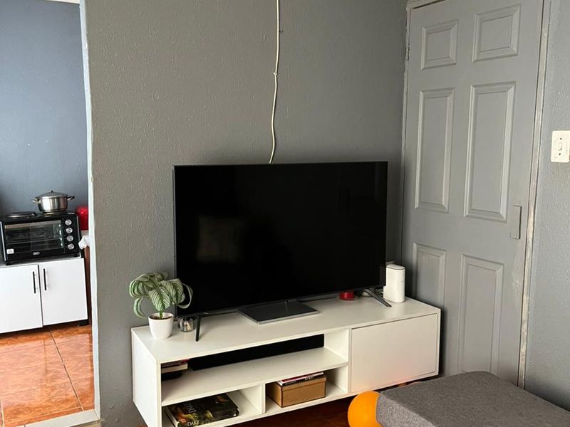 A living room area featuring tiled flooring and a panel door, with visible ceiling trim and electrical wiring requiring maintenance.