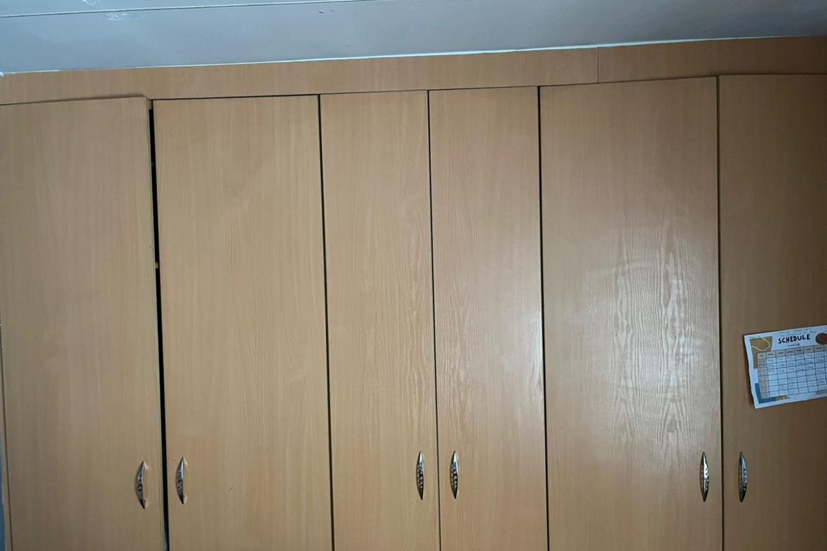 A bedroom featuring floor-to-ceiling built-in wooden cupboards with integrated handles.
