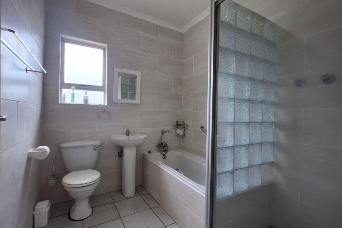 A clean, neutral-toned bathroom featuring a pedestal basin, toilet, bathtub, and a separate shower enclosure with a decorative glass block wall.