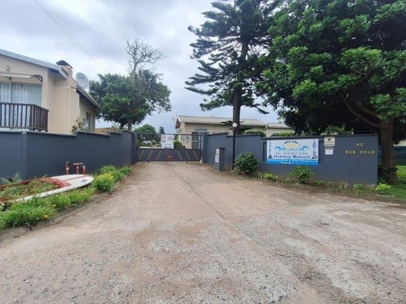 Front entrance view of the property featuring a paved driveway, boundary wall, and security gate access.
