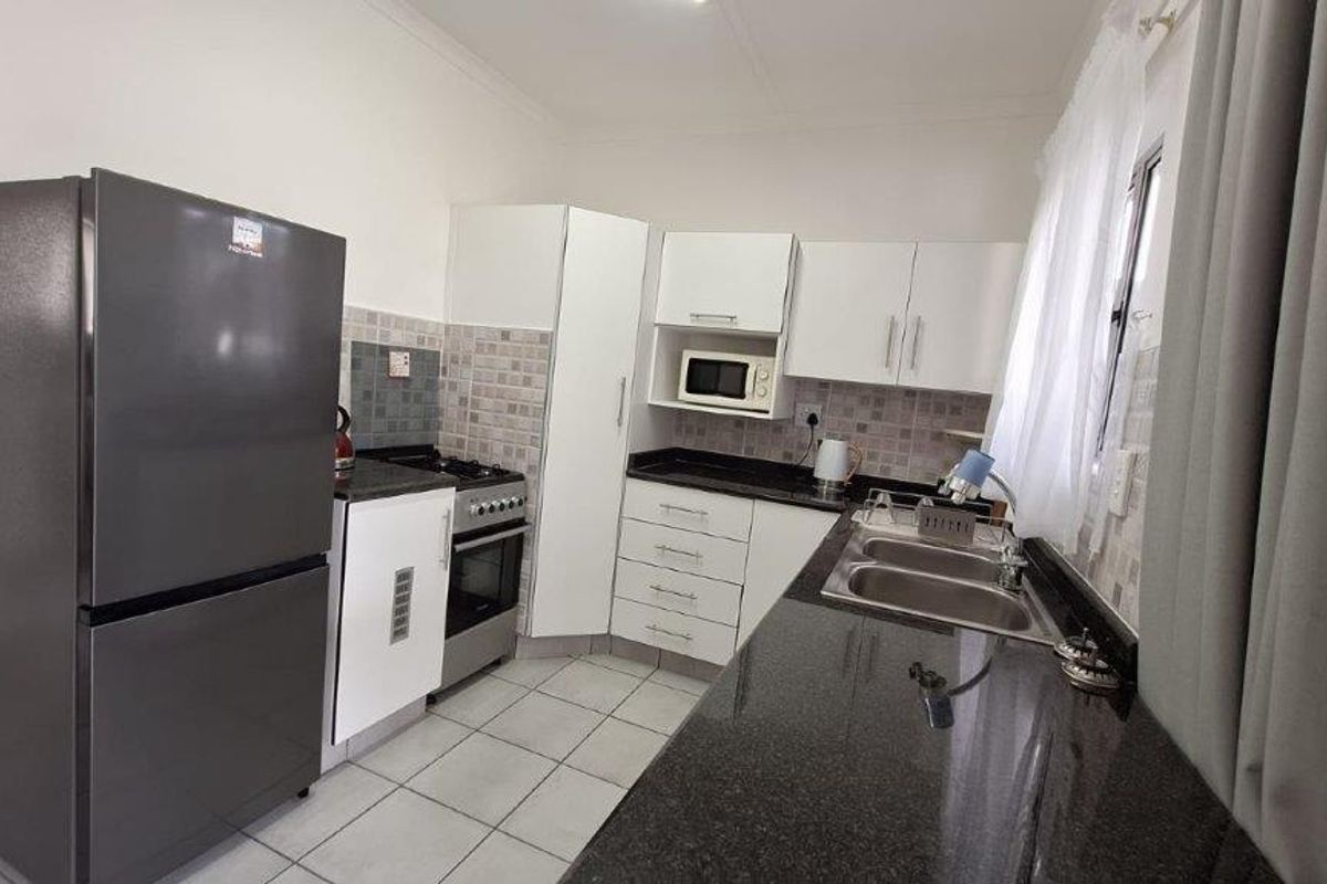 A functional kitchen featuring granite countertops, white cabinetry, a double basin sink, and a built-in oven with a gas hob.