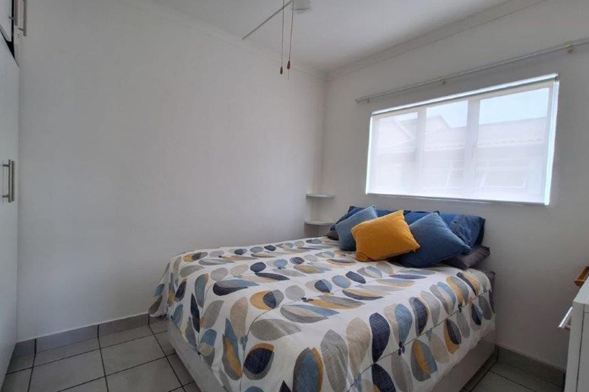 A neat bedroom featuring tiled flooring, built-in cupboards, and a roller blind, providing a functional and well-maintained living space.