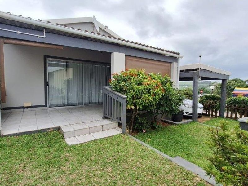 A covered patio area with tiled flooring and sliding glass door access, overlooking a private garden space.