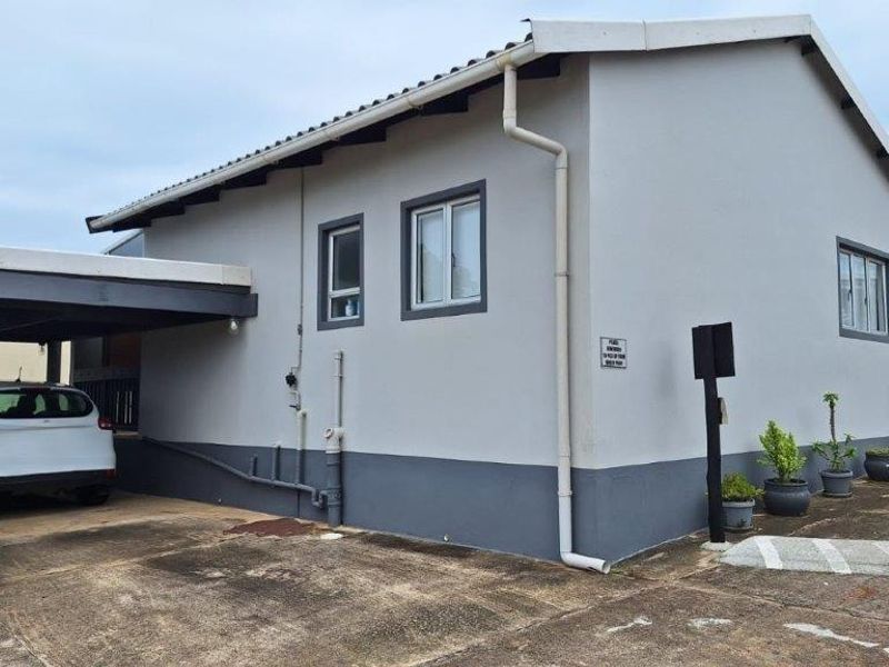 Exterior view of a townhouse featuring a covered carport, concrete driveway, and neutral grey painted facade with aluminium window frames.