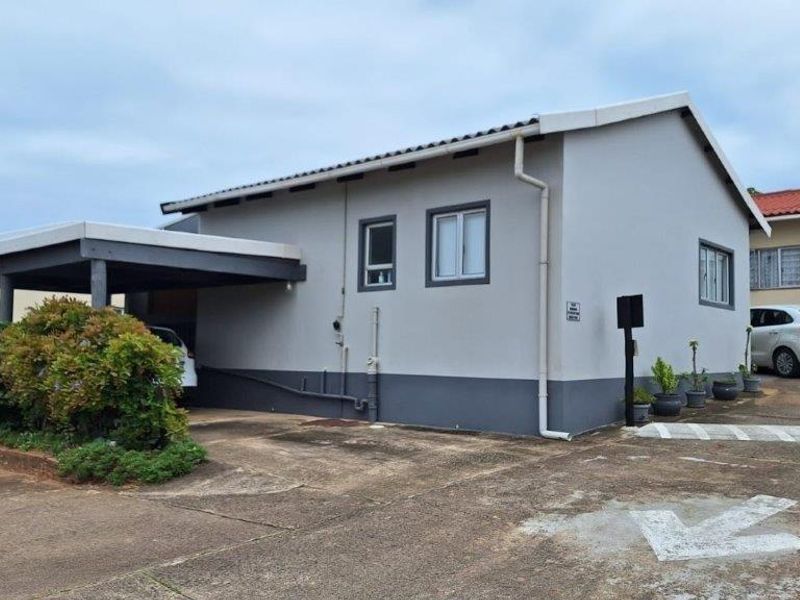 Side profile of a townhouse featuring a covered carport, concrete driveway, and neutral exterior paint finish with visible guttering and downpipes.