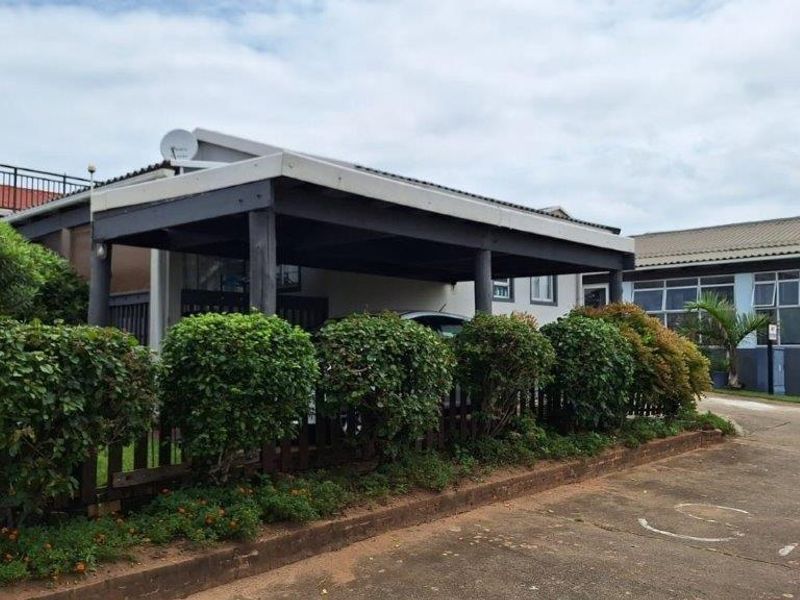 Front exterior view of the townhouse featuring a covered carport, timber fencing, and a concrete driveway with established garden hedging.