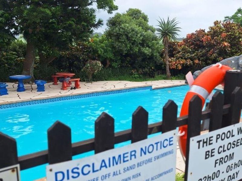 Outdoor swimming pool area featuring a safety fence, paved surround, and landscaped garden backdrop.