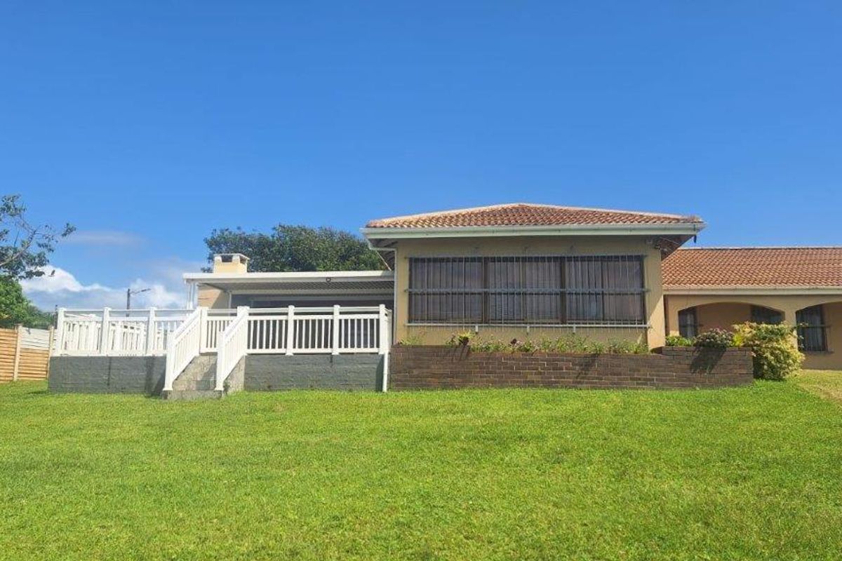 Rear view of the property featuring a raised deck with white balustrades, a brick retaining wall, and a tiled roof.