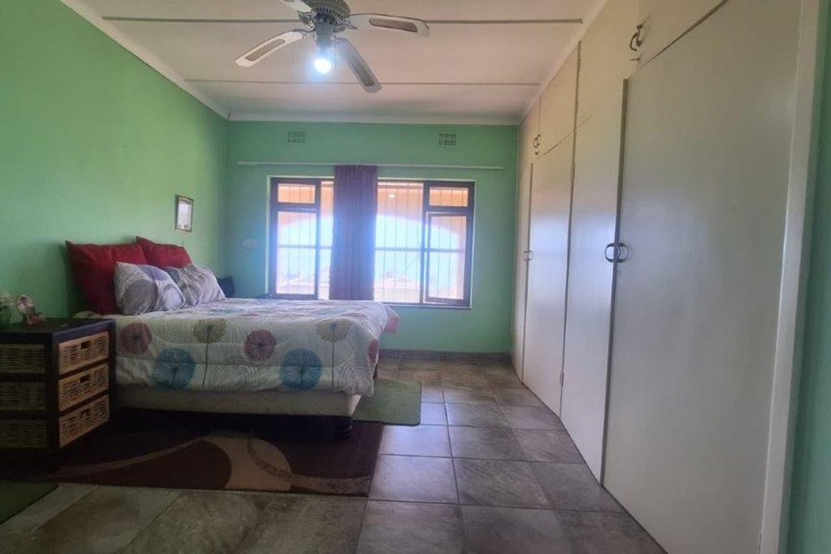 A bedroom featuring tiled flooring, a ceiling fan, and extensive built-in cupboard storage with security bars on the windows.