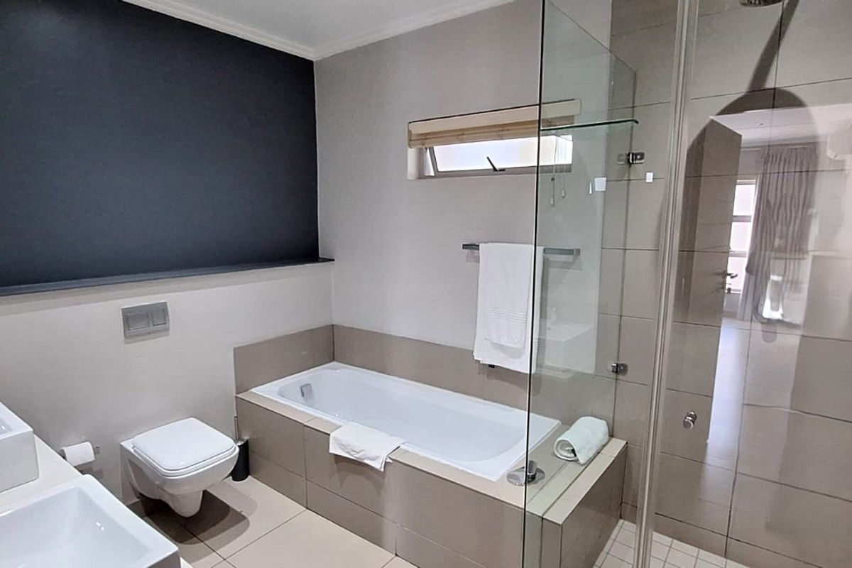 Modern bathroom featuring a double vanity, wall-hung toilet, built-in bathtub, and a separate glass-enclosed shower with neutral tiling.