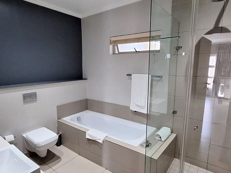 Modern bathroom featuring a double vanity, wall-hung toilet, built-in bathtub, and a separate glass-enclosed shower with neutral tiling.