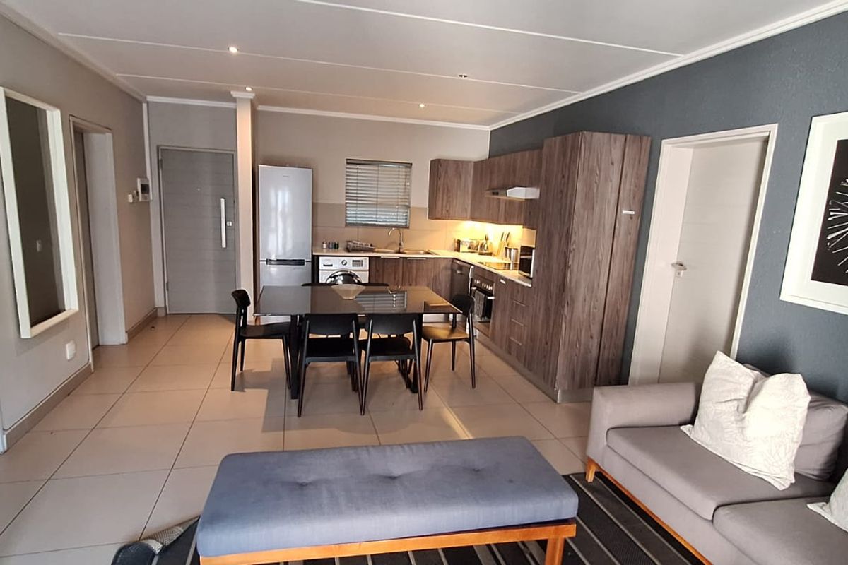 Modern open-plan living area featuring a well-appointed kitchen with wood-finish cabinetry, integrated appliances, and sleek tiled flooring throughout the space.
