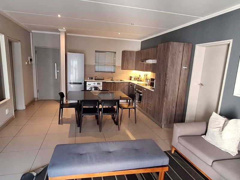 Modern open-plan living area featuring a well-appointed kitchen with wood-finish cabinetry, integrated appliances, and sleek tiled flooring throughout the space.