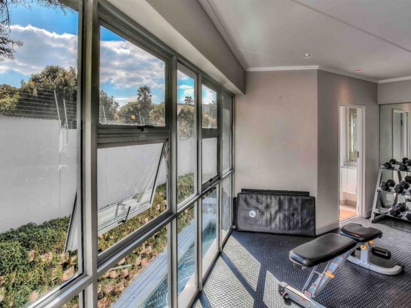 A well-lit home gym featuring durable rubberized flooring, a full-length mirrored wall, and large windows providing natural light and views of the exterior.