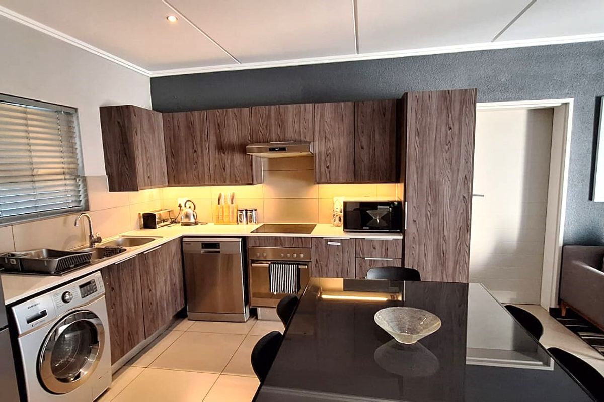 Modern open-plan kitchen featuring wood-grain cabinetry, stainless steel appliances, and tiled flooring, seamlessly integrated with the living area.