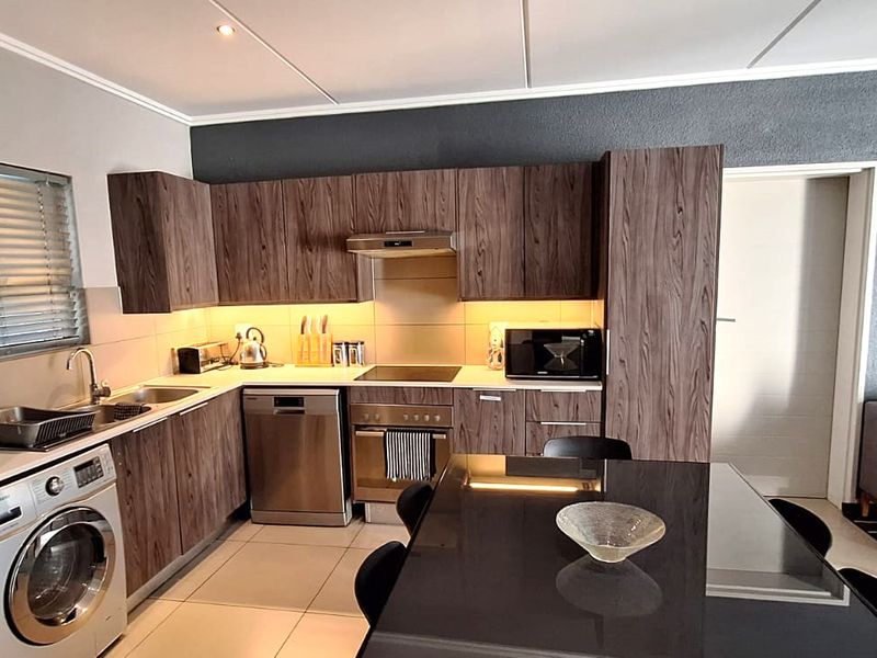 Modern open-plan kitchen featuring wood-grain cabinetry, stainless steel appliances, and tiled flooring, seamlessly integrated with the living area.