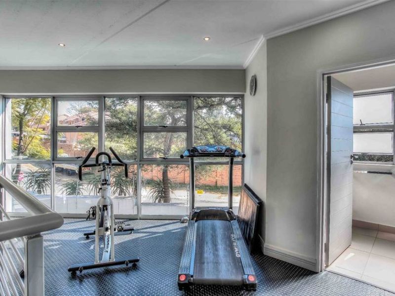 A bright gym area featuring large windows, recessed lighting, and tiled flooring, overlooking the exterior surroundings.