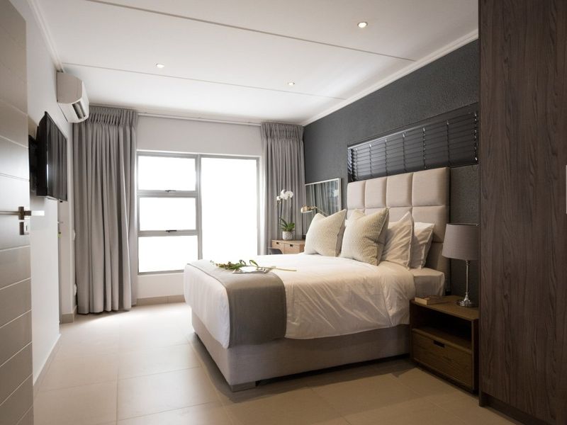 A well-appointed bedroom featuring tiled flooring, built-in cupboards, recessed downlighting, and an integrated air conditioning unit.