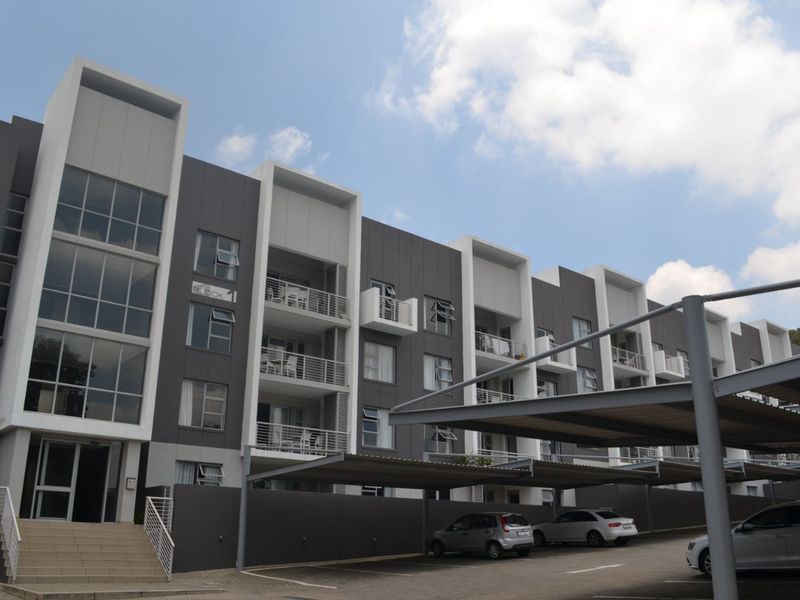 Modern multi-story apartment complex featuring contemporary grey and white facade, private balconies, and dedicated covered parking bays.