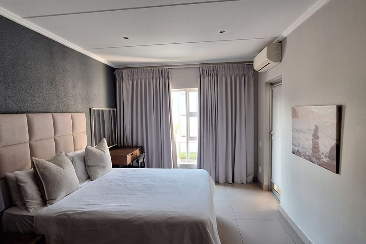 A well-maintained bedroom featuring tiled flooring, recessed downlighting, a wall-mounted air conditioning unit, and access to an outdoor area via a sliding door.