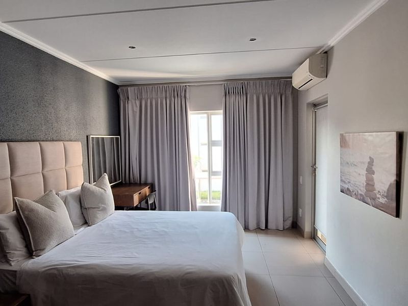 A well-maintained bedroom featuring tiled flooring, recessed downlighting, a wall-mounted air conditioning unit, and access to an outdoor area via a sliding door.